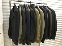 View of ten men's suit jackets hanging on a rack showing variety of colors and fabrics.
