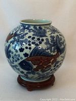 Front view of round porcelain jar with blue and rust koi fish and foliage pattern on wooden stand.