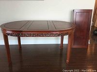Full view of oval rosewood table with leaf stored vertically beside