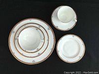 Photo showing set of dinnerware including plates, cups, and saucers with gold and silver decorative trim.