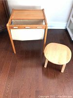 Front view of vintage teak side table with fabric magazine sling and a small wooden stool next to it.