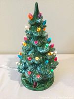 Front view of the vintage ceramic Christmas tree showing multicolored bulbs lit and the detailed ceramic branches and base.