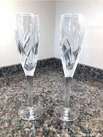 Two Waterford crystal champagne flutes placed side by side on granite countertop showing overall condition and shape.