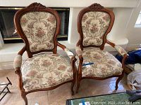 Front view of two queen anne style chairs showing carved wood frames and floral upholstery on seats and backs.