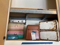Storage trunk with rust and wear inside, vintage brown and white vanity cases, silver metal briefcase visible on metal shelving.