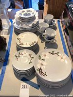Stack of white ceramic plates and saucers with white flower and branch design, alongside blue floral patterned cups and plates.