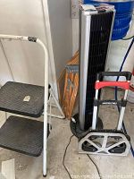 Photo showing Bionaire tower fan, Cosco step stool, small wooden step stool, and Magna Cart folding cart (not included in lot) in garage.