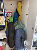 Photo of camping gear stored in a cupboard including sleeping bags, first aid kit, camping chairs in carry bags and citronella candles