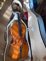 Full view of cello seated in open beige plush-lined gray molded hardshell case.