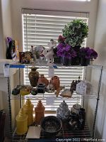 Photo of multiple shelves with novelty clocks, art glass angel figurine, various jars, vases, and figurines