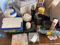 Photo of coolers, thermos, power drill, gloves, cleaning supplies, hardware, and light bulbs on a table.