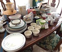 Wide angle view of table showing all items including stacked plates, bowls, mugs, and the ceramic wash basin and jug set.