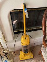 Full view of the yellow Eureka Wide Track Lite vacuum cleaner standing upright, showing its handle, transparent dust container, and power cord.