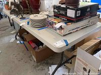 White folding table with various items on top, including plates and boxes, showing overall use and surface.
