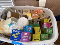 Basket containing assorted boxes of plastic wraps, zipper seal bags, and paper party supplies such as disposable cups and plates.