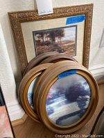 View of all framed prints stacked against wall showing one rectangular frame with prayer text and four oval landscape prints.