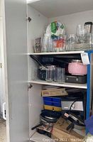 Photo of cabinet shelf containing assorted glassware, pans, and kitchen items