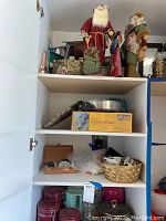 Photo of upper shelves showing Christmas figurines and pottery wheel box with other household items.