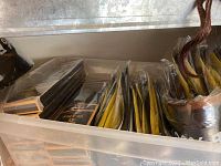 Clear plastic storage bin filled with multiple sealed packages of hair extensions with black and yellow labels and packaging.