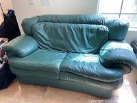 Front view of a green faux leather loveseat showing creased cushions and some wear marks