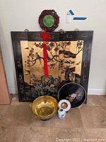 Four Asian-style panels with gold backgrounds and bird/floral motifs, lacquer tray, brass bowl, vase, and Chokin gold plaque arranged on floor.
