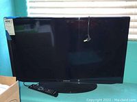Front view of Samsung 32-inch TV showing screen, bezel, and base stand with remote placed underneath.