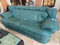 Full front view of green faux leather sofa placed on tiled floor with visible wear on upholstery.