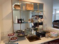 Wide view showing glass jars, decorative plates, stemware, serving trays, and kitchen rack near sink