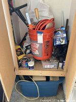 Photo showing a variety of tools in an orange Home Depot bucket, with several cans and bottles nearby, and a large blue bin underneath containing cords or hoses.