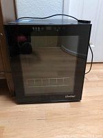 Closed view of black Vinotemp wine fridge with glass door and control panel on top front edge.