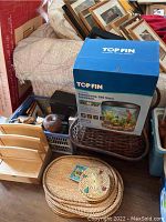 Photo showing the top of the brown wicker basket, aquarium box, wooden apple and lion figurine, photo box and placemats.