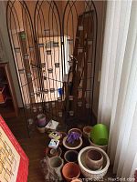 Front view of black metal wall divider holding multiple small candle pots with assorted plant pots and aromatherapy kit on floor nearby.