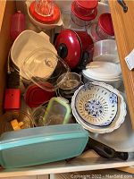 Overview of mixed glass, plastic, and metal cookware including storage bowls, mixing bowls, measuring cup and covered pots in various colors including red, turquoise, and white.