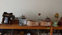 Top shelf view displaying two ceramic cats, two glass lamps, four decorative vases, and boxed Mikasa glass plates.
