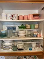 Full cupboard shelf with mugs, plates, bowls, glasses, and trays in various colors and materials