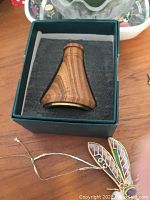 Wooden small vessel in a green box with colorful dragonfly clip in front on wooden surface.