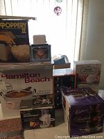 Overview of various kitchenware items including Hamilton Beach slow cooker, popcorn machine box, food chopper, Cadbury chocolate fountain, and other boxed kitchen tools.