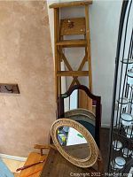 Wooden step ladder with multiple visible scratches and stacked decorative mirrors in front