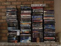 Large assortment of DVDs and some VHS stacked against brick wall including TV series, movies, and some Wii games.