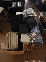 Photo showing stacks of CDs, vinyl records in a basket, some books, and digital alarm clock on a table.