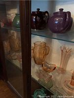 Glass cabinet shelf with various pink glassware including pitcher, vases, small bowls, and a clear cut glass shoe.