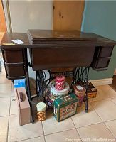 Front angled view of vintage Singer sewing machine table with assorted storage tins underneath and lockbox beside it.
