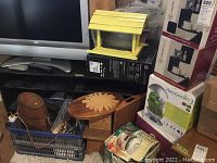 Photo showing the yellow wooden bird feeder on top of wooden decor items and a crate filled with cutlery underneath television.