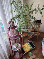Photo showing multiple small tables, a large potted Benjamin Ficus tree, and a decorative cloth doll placed on one of the tables.