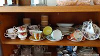 Shelf displaying assorted bone china teacups, saucers, and plates with various floral patterns and colors.
