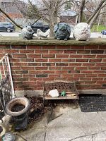 Full view showing four animal figurines on brick ledge, metal decorative bench below, and outdoor black urn on ground.