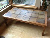 Rectangular coffee table with wood frame and legs. Top surface has 18 square tiles with fern patterns in natural earthy tones. Table measures approximately 52x28x16.5 inches.