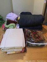 Entire lot of bedding items including sleeping bags, blankets, comforter set, and sheets arranged on the floor.