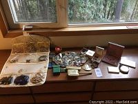 Wide view of dresser top showing hanging jewelry organizer, round tray with assorted earrings, beads and pins, jewelry boxes, and boxes for smoking items and brush set