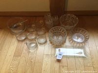 Lot of multiple crystal and glass bowls arranged on wooden floor including large salad bowl and smaller bowls with one glass serving utensil